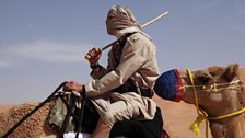 James Cracknell with face covered by scarf riding camel in the Empty Quarter, Oman.