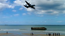 A plane flies over the beach at Arromanches