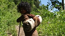 A Raute child migrates from camp to camp with a small load on her back