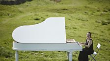 Katie Buttermere plays a white grand piano in a field