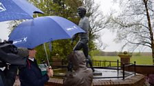 Norma Morton and presenter Alex are discussing Jim’s love of the rain next to his statue in Hill O’Beath