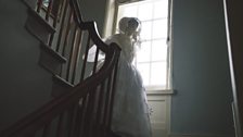 Charlotte Bronte descends the stairs in wedding dress and veil