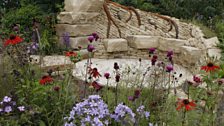 A weathered steel and stone seating area provides shelter.