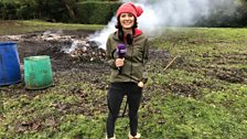 Julie warms herself by the smouldering remains of the bonfire at the starting point in Corpusty