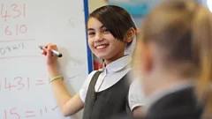 A smiling primary school pupil writes the solution to a maths puzzle on a whiteboard