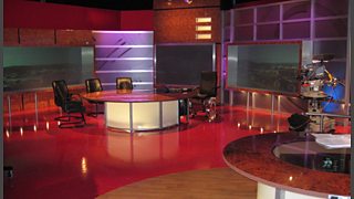 A studio with three chairs around a desk, with subdued lighting.