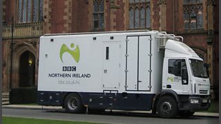 A white truck parked outside a gothic building.