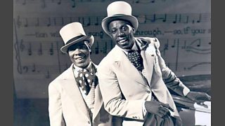 Two black singers in white coats, spotted cravats and top hats.