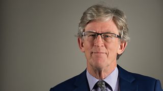 A man in glasses wearing a navy blue suit