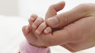 Adult hand holding a young baby's hand