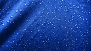 A close-up of dark blue, shiny nylon fabric repelling water droplets.