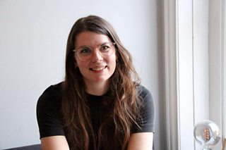 Designer, Marie Rasmussen looking slightly off from the camera smiling and wearing glasses and a black top.