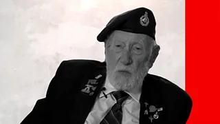 A elderly man wearing a black suit looks at the camera