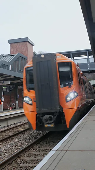 An orange train pulling into a station