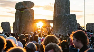 The sun peeks through the stones at Stonehenge as a crowd watches