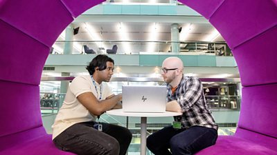 Dau gydweithiwr BBC yn siarad mewn pod swyddfa fodern