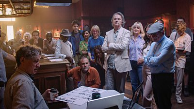 A group of participants stand around a screen in the Queen Vic pub while filming
