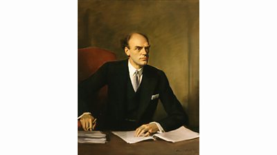 Portrait of John Reith seen at his desk signing papers. He looks characteristically serious.