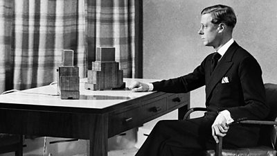 King Edward VIII sits at a desk with two box-like microphones on the surface.