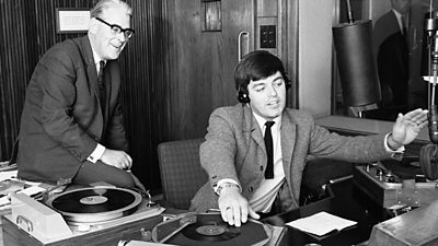 Robin Scott sits on the desk as DJ Tony Blackburn spins a disc.