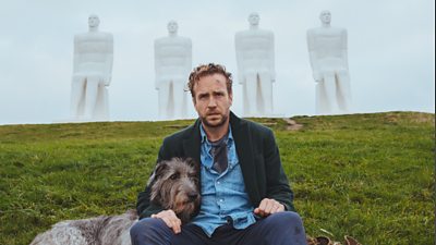 Rafe Spall looks dishevelled sitting next to a Danish statue, his arm around an equally sad looking Irish Wolfhound
