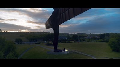 A man watches television at the feet of the Angel of the North