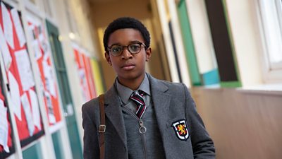 A young black boy in school uniform in a corridor