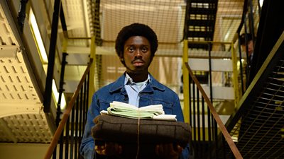 A young black man carries a bundle of linen inside a prison