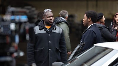 Director Steve McQueen on set with John Boyega as Leroy Logan getting out of a car