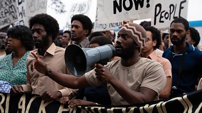 Malachi Kirby as Darcus Howe with a megaphone at a demonstration