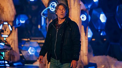 John Bishop's Doctor Who character Dan stands in the TARDIS in a black jacket and jeans. He looks overwhelmed by the size and scale of the TARDIS interior.