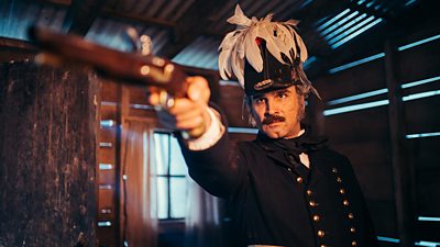 A man in military uniform and a feathered helmet points a gun at something off screen.