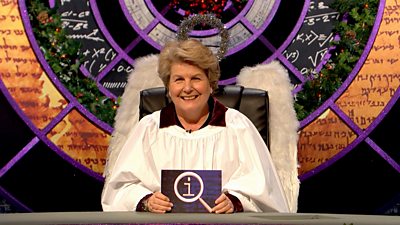 QI presenter Sandi Toksvig sits at her desk dressed as an angel with large silver wings