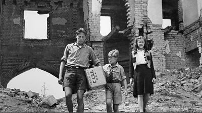 Three siblings in a bombed out building with care parcels