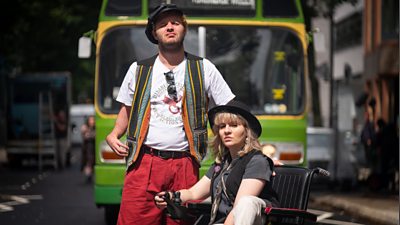 Arthur Hughes as Alan Holdsworth and Ruth Madeley as Barbara Lisicki, in front of a bus