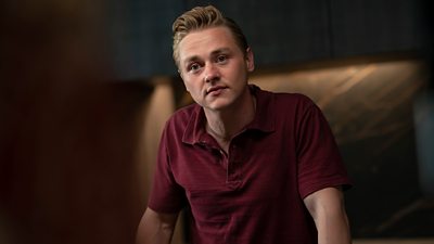 Ben Hardy plays Simon in The Girl Before. He wears a dark maroon coloured short sleeve shirt.