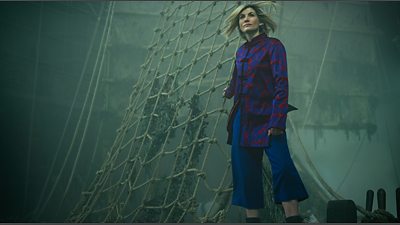 The Doctor (Jodie Whittaker) stands on the side on a ship, holding on to the nets in Doctor Who's Legend of The Sea Devils