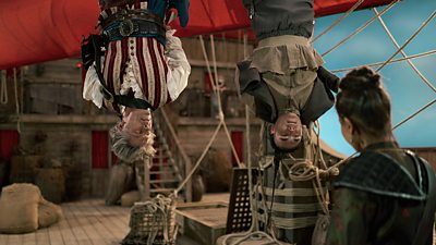 Dan Lewis (John Bishop) and Ying Ki (Marlow Chan Reeves) hand upside down, captured on board a ship.