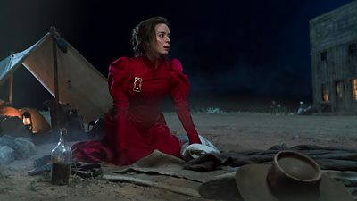 Emily Blunt is pictured on the ground at night, looking slightly shocked or startled