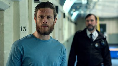 Tommy (James Norton) stands in the corridor outside his cell - a prison guard is visible in the background