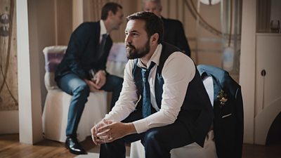 Jimmy (Martin Compston) sits on a chair at a wedding holding a glass