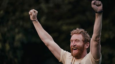 Tully (Tony Curran) cheers with his arms outstretched