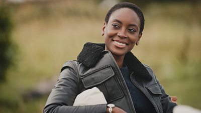 Iona (Tracy Ifeachor) smiles as she sits outdoors