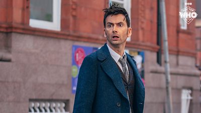 David Tennant as the Doctor in Doctor Who's 60th Anniversary specials - he stands on the street in daylight looking shocked