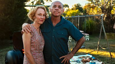 David Field as Dean and Sophie Gregg as Tina - they stand at a barbecue with a swing in the background