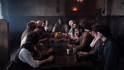 A group of men and women sit around a large table in a pub having a discussion