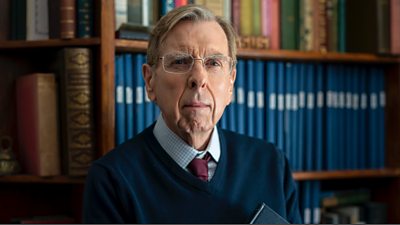 Timothy Spall as Peter Farquhar, an older gentleman wearing glasses standing in front of a bookcase