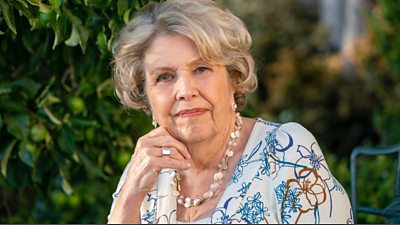 Anne Reid as Ann Moore Martin, an older lady wearing a floral patterned top