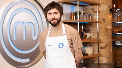 James Buckley wearing MasterChef apron and masterchef m in background