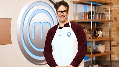 Marcus Brigstocke wearing masterchef apron with masterchef m in background